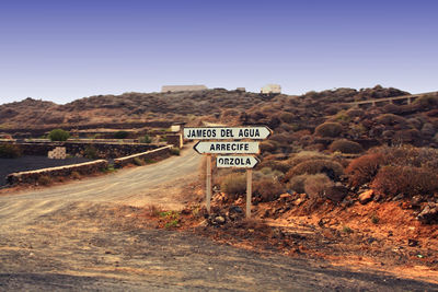 Information sign on road by plants against sky