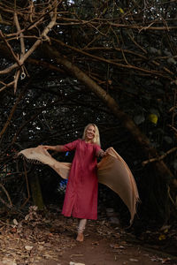 Portrait of young woman standing against tree