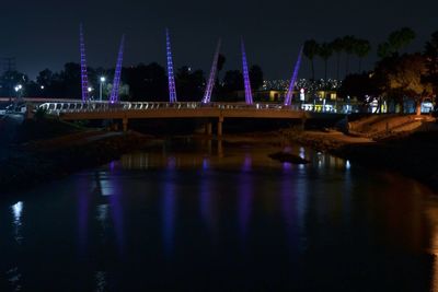 Illuminated bridge over river in city at night