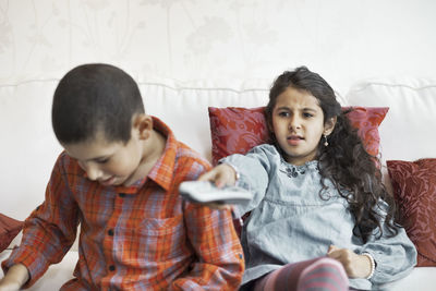 Girl watching tv while sitting with brother in living room