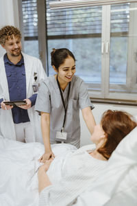 Smiling nurse talking to senior female patient lying on bed by doctor in hospital