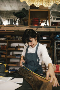 Smiling female entrepreneur measuring wood in upcycling workshop