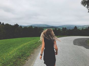 Rear view of woman tossing hair while walking on road against sky