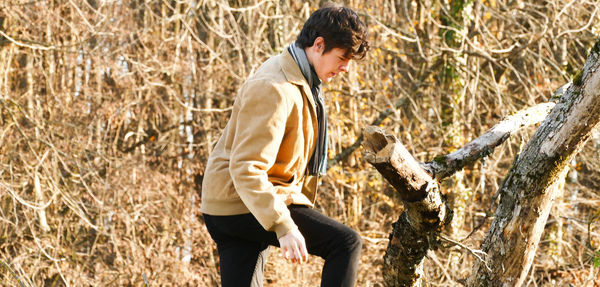 Side view of young man walking against bare trees