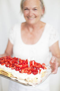 Senior woman holding strawberry cake, studio shot