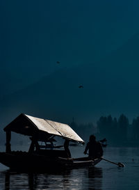 Silhouette man sitting in boat on lake against sky