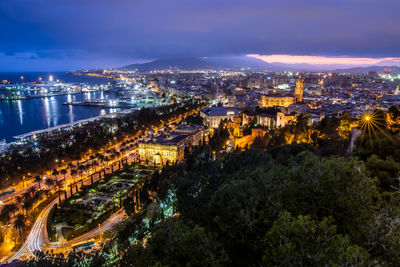 High angle view of illuminated city by sea against sky