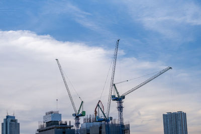 Low angle view of cranes and buildings against sky