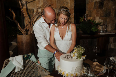 Midsection of bride and groom cutting cake