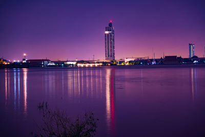 Illuminated buildings by river against sky at night