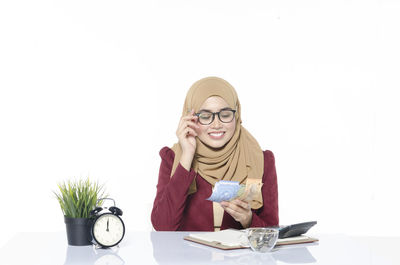 Woman holding book while standing against white background