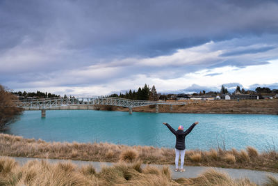 Tourist pose at the maclaren foot bridge in late winter with beautiful turquoise color lake tekapo.