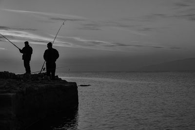 Men standing on rock formation while fishing at lake