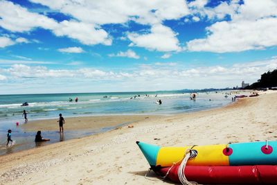 People and water sled at beach against cloudy sky