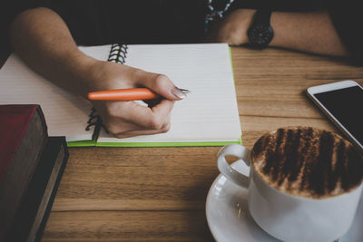 A woman writes a report on a table with a cup of coffee.