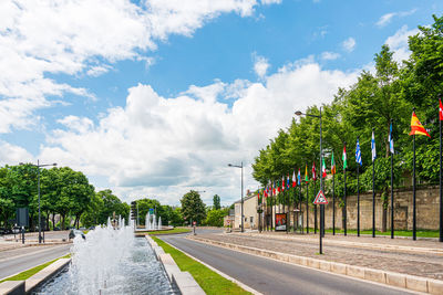 Road by trees against sky in city