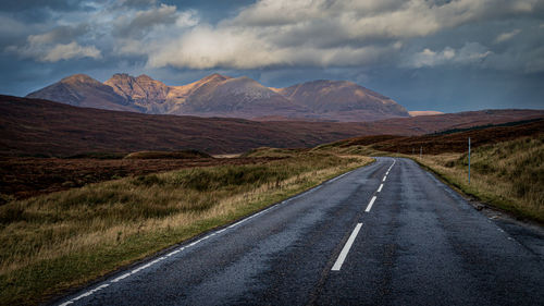 Empty road by mountains against sky