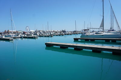 Sailboats moored at harbor against clear blue sky