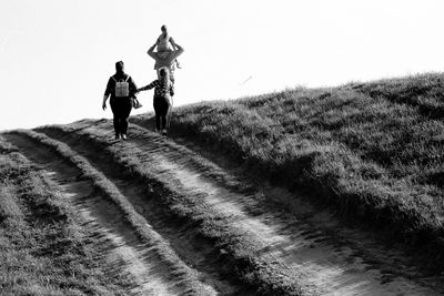 Rear view of people walking on street amidst field