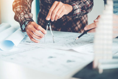 Midsection of engineer with colleague drawing on blueprint