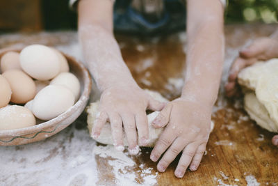 Cropped hands of mother and son kneading dough on wooden table at yard