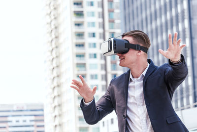 Smiling businessman gesturing while wearing virtual reality in city