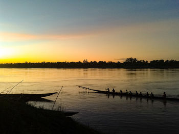 Silhouette people in boat on lake against sky during sunset