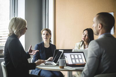 Senior businesswoman discussing strategies with colleagues while sitting in board room