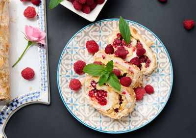 Baked meringue roll with cream and fresh red raspberry on a black wooden board, delicious dessert