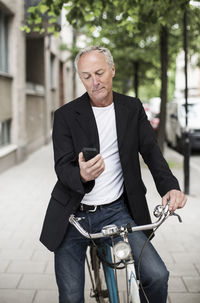 Businessman using mobile phone while sitting on bicycle at sidewalk