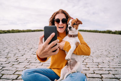 Smiling woman taking selfie while sitting with dog outdoors