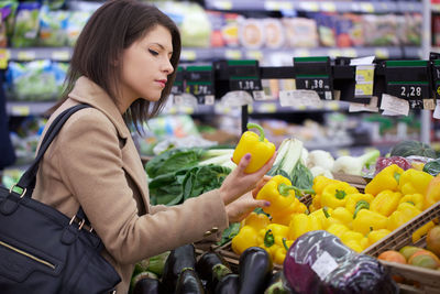 Side view of young woman holding yellow bell pepper in store