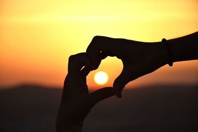 Close-up of silhouette hand holding sun during sunset