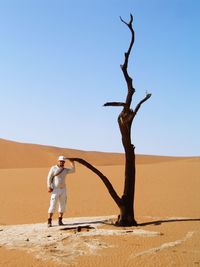 Full length of man standing by bare tree on desert against clear sky