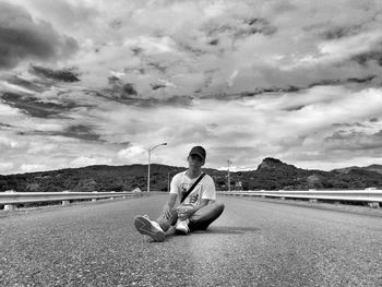 Man sitting on road against sky