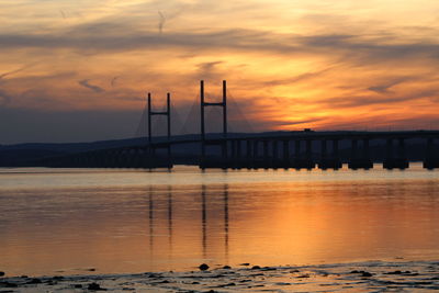 Bridge over sea against orange sky