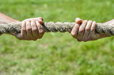 Close-up of hands holding rope on field