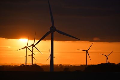 Silhouette wind turbines on landscape against sky during sunset