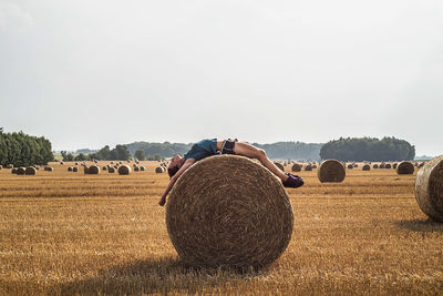 Side view of man lying on haye bale against sky