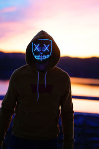 Man wearing neon mask while standing against orange sky