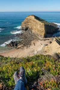 Low section of person on rock at beach against sky