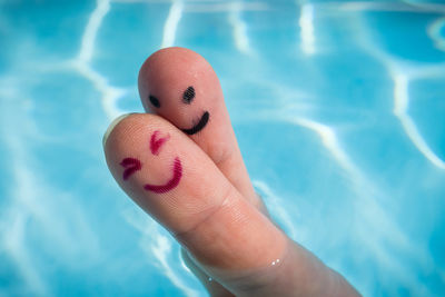 Cropped fingers of person with anthropomorphic faces in swimming pool