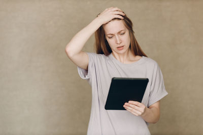 Young woman using digital tablet while standing against wall