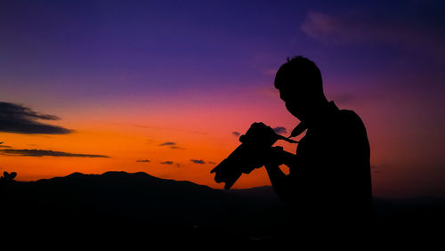 Silhouette man photographing against sky during sunset