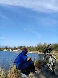 Rear view of woman with hijab sitting on shore against blue sky