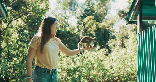 Young woman standing by plants against trees