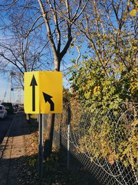 Road sign by tree against sky