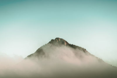 Scenic view of mountain amidst mist against clear sky