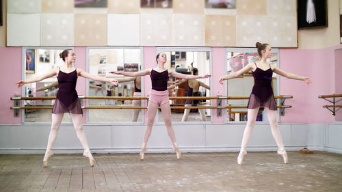 In dancing hall, young ballerinas in black leotards perform pas echappe, standing on toes in pointe 