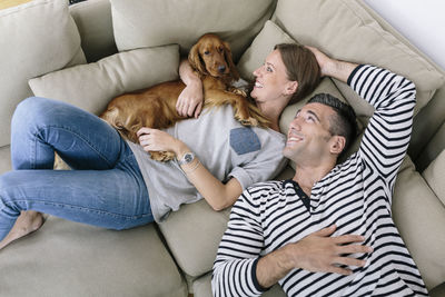 Smiling couple with dog lying on couch